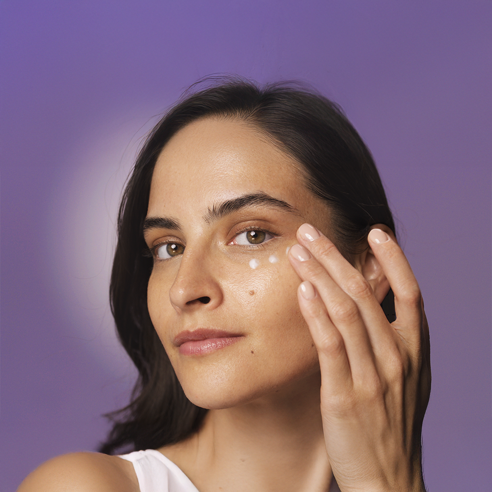 En kvinna applicerar HL/Skin Nourishing Eye Cream på sitt ansikte.